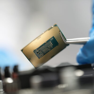 The master is holding a chip over the device with tweezers, close-up, blurry. Microcircuit in the electronics industry